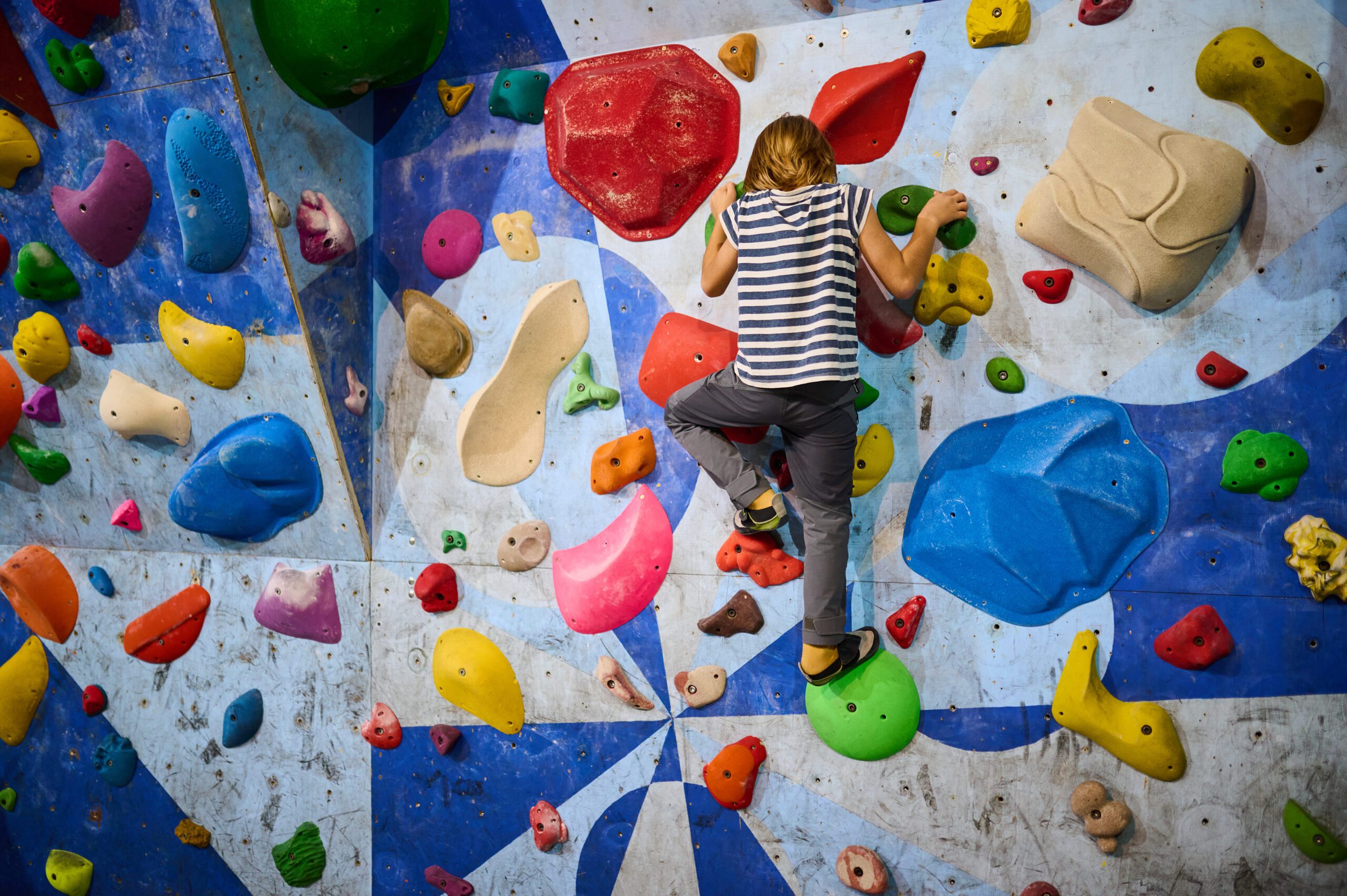 A child rock climbing on an indoor bouldering wall with colorful holds, making it a perfect activity spot for children's birthday party venues in Dublin.