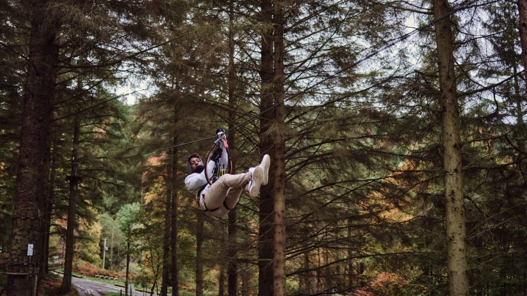 A person ziplining through a forest with tall trees in the background.