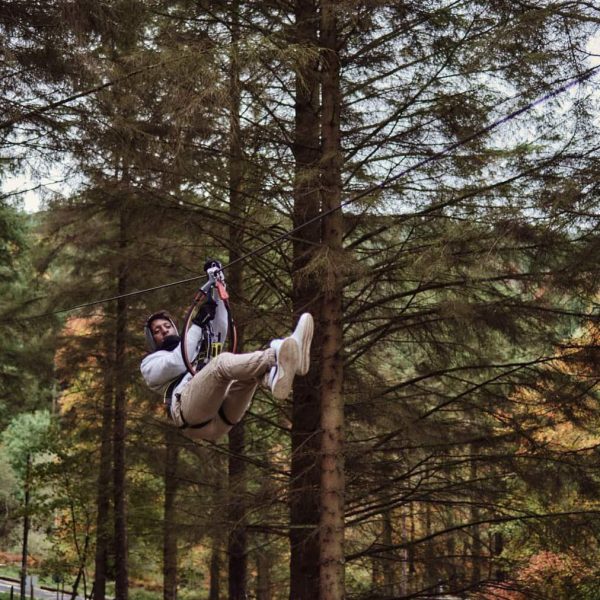 A person ziplining through a forest with tall trees in the background.