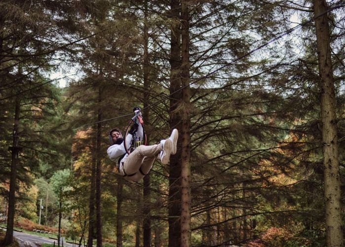 A person ziplining through a forest with tall trees in the background.