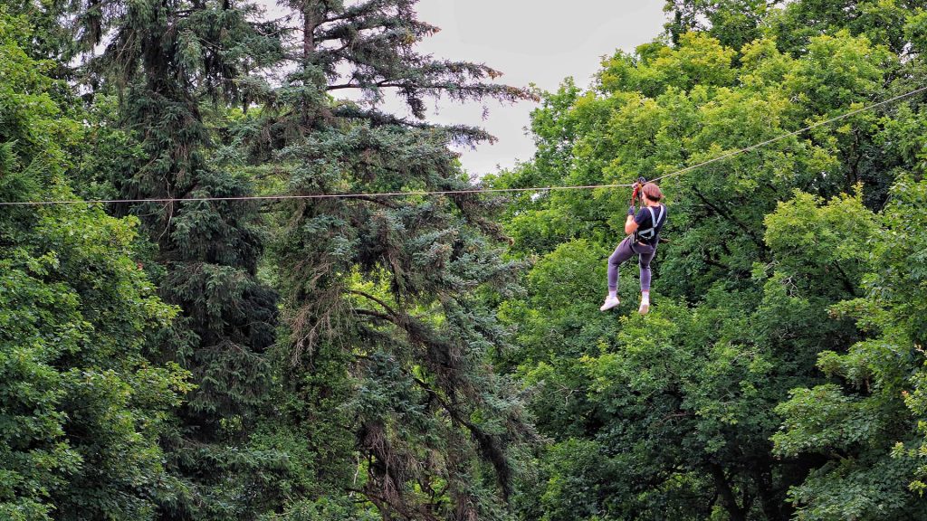 A person zip-lining through a dense green forest.