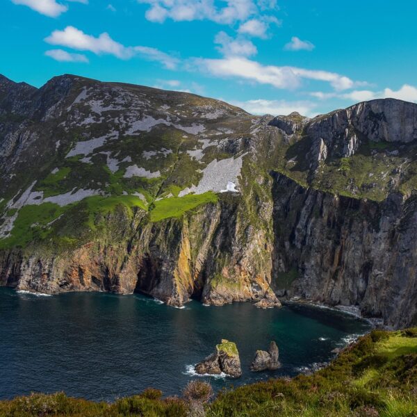 Experience the mesmerizing cliffside view of Slieve League in Ireland, perfect for a family travel adventure. Marvel at steep rocky cliffs and green patches against the ocean backdrop, all under a serene blue sky, offering one of the best Ireland outdoor escapes for your spring break adventures.