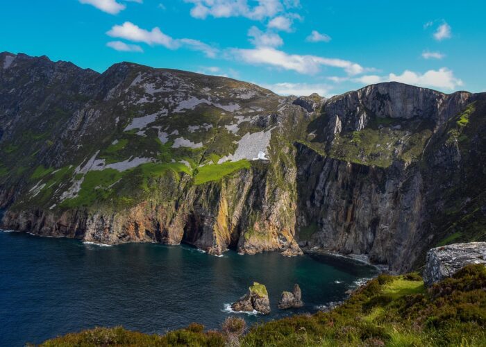 Experience the mesmerizing cliffside view of Slieve League in Ireland, perfect for a family travel adventure. Marvel at steep rocky cliffs and green patches against the ocean backdrop, all under a serene blue sky, offering one of the best Ireland outdoor escapes for your spring break adventures.