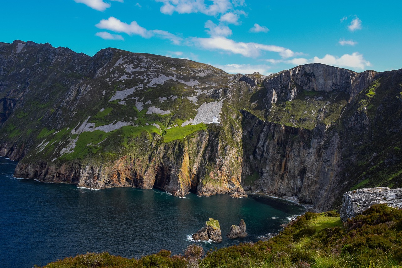 Experience the mesmerizing cliffside view of Slieve League in Ireland, perfect for a family travel adventure. Marvel at steep rocky cliffs and green patches against the ocean backdrop, all under a serene blue sky, offering one of the best Ireland outdoor escapes for your spring break adventures.