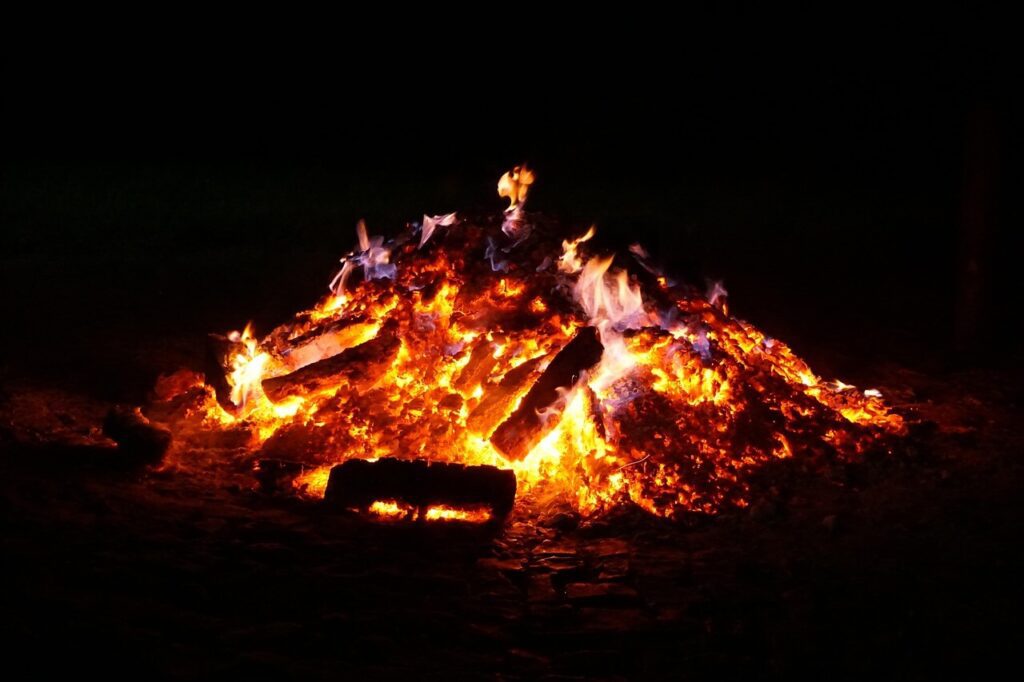A large bonfire with glowing embers and flames burning wooden logs at night, illuminating the surrounding darkness—a magical scene from Summer Solstice Ireland, celebrating the longest day of the year.