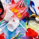 Assorted single-use plastic items, including cups, plates, cutlery, straws, and bottle caps, are scattered on colored plastic bags—highlighting the urgency for change by 2025 and reflecting on the spirit of World Environment Day.