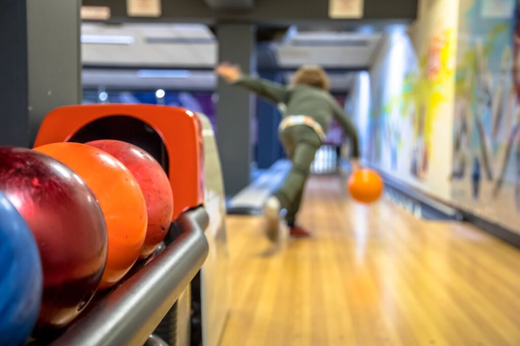 A person bowls with an orange ball on a wooden lane as colorful bowling balls sit in the foreground—perfect inspiration for active kids parties or teen birthday parties.